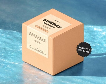 Può includere: Una scatola di cartone marrone con un'etichetta bianca che dice "SUNDAY MORNING" in caratteri neri. L'etichetta dice anche "NATURAL COCONUT SOY WAX CANDLES" e "GRAPEFRUIT & MINT". La scatola è su una superficie blu.