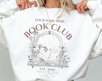 May include: White sweatshirt with a brown graphic design that says "YOUR NAME HERE BOOK CLUB EST. 2024". The graphic features a floral archway with a book underneath.