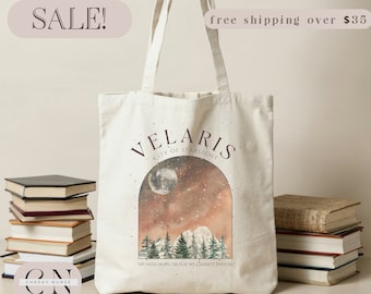 May include: A white canvas tote bag with a brown and gold design featuring a moon, stars, and a forest scene. The text "VELARIS CITY OF STARLIGHT" is printed in brown on the bag. The quote "WE NEED HOPE, OR ELSE WE CANNOT ENDURE" is printed in brown at the bottom of the bag.