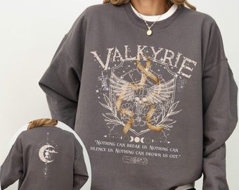 Może przedstawiać: Szara bluza z nadrukiem graficznym przedstawiającym skrzydlatą tarczę z napisem "VALKYRIE" nad nią. Grafika zawiera również półksiężyc, gwiazdy i tekst "NOTHING CAN BREAK US. NOTHING CAN SILENCE US. NOTHING CAN DROWN US OUT."