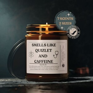 Puede incluir: Una vela de vidrio marrón con una etiqueta blanca que dice "Smells Like Quizlet and Caffeine". La vela está encendida y tiene una tapa dorada. La etiqueta también incluye un pequeño símbolo médico y un estetoscopio.