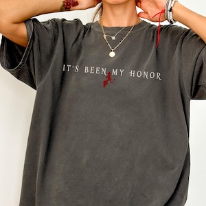 May include: A dark grey t-shirt with the text "It's Been My Honor" printed in white. A small red dragon graphic is centred below the text.
