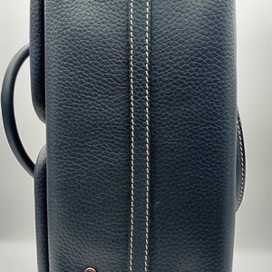 May include: A navy blue leather briefcase with white stitching details. The briefcase has a textured surface, a handle, and metal hardware. The design includes a vertical white stitch detail down the center.