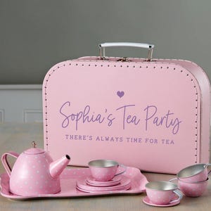 May include: A pink polka-dot tea set with a matching teapot, tray, cups, and saucers. The set is displayed in front of a pink suitcase with the text "Sophia's Tea Party" and "There's Always Time For Tea."