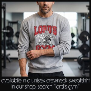 Puede incluir: Una sudadera gris jaspeado de cuello redondo con un estampado gr&aacute;fico que incluye el texto rojo "LORD'S GYM" y una ilustraci&oacute;n en blanco y negro de una figura cargando una cruz de madera con el texto "THE SIN OF THE WORLD" en el centro.