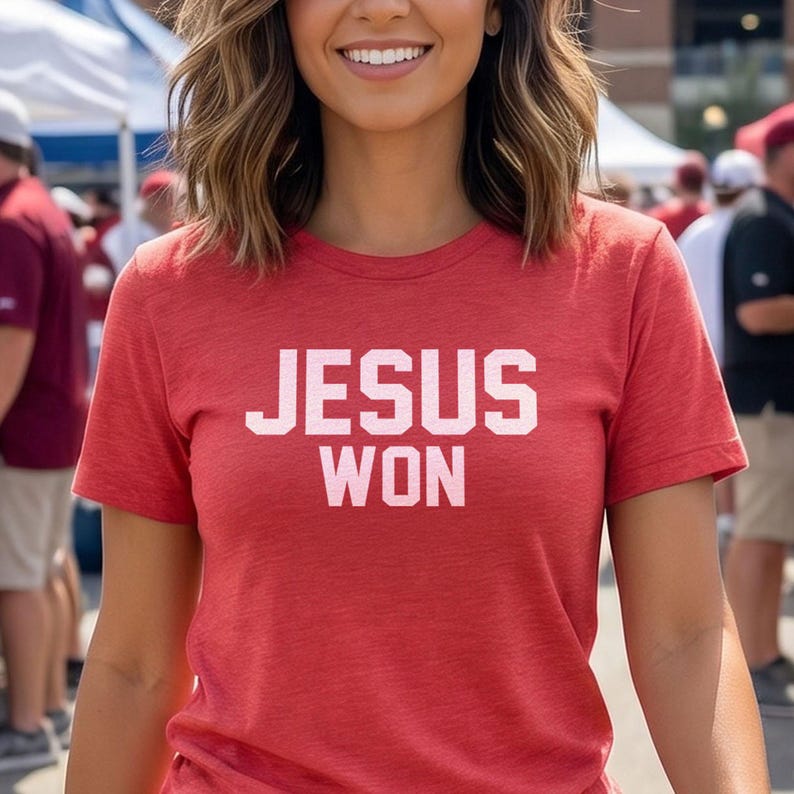 May include: A red short-sleeved crew neck t-shirt featuring the text JESUS WON printed in a bold, white, block-style font across the chest. The fabric has a subtle heathered texture, and the garment is designed with a standard fit and hem.