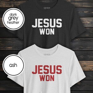 May include: Two short-sleeve crew neck t-shirts. The top shirt is dark grey heather with white text that reads JESUS WON. The bottom shirt is ash grey with red text that reads JESUS WON. Both shirts feature the brand name Genesis at the neck.
