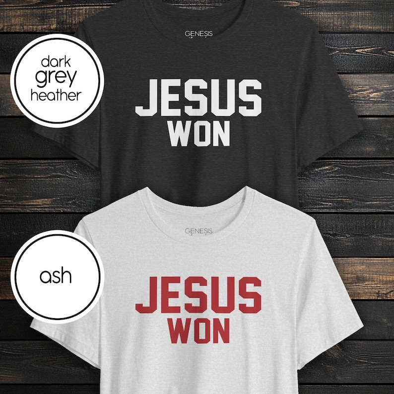 May include: Two short-sleeve crew neck t-shirts. The top shirt is dark grey heather with white text that reads JESUS WON. The bottom shirt is ash grey with red text that reads JESUS WON. Both shirts feature the brand name Genesis at the neck.