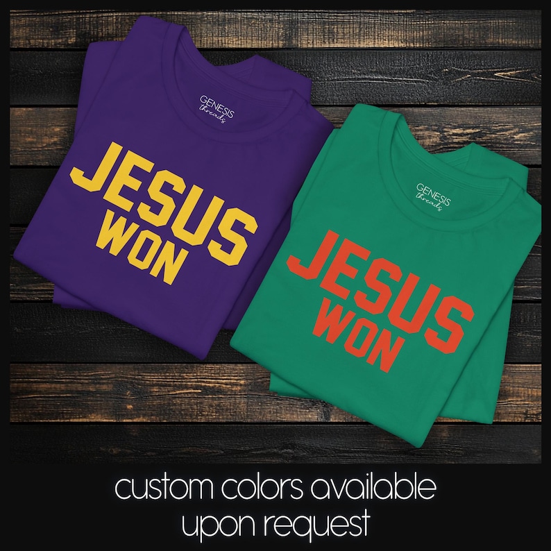 May include: Two short-sleeved crew neck t-shirts. One is purple with yellow text reading JESUS WON, and the other is green with orange text reading JESUS WON. Both shirts feature a Genesis Threads brand label printed on the inside neck area.