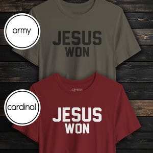 May include: Two short-sleeve crew neck t-shirts. The top shirt is army green with black text that reads JESUS WON. The bottom shirt is cardinal red with white text that reads JESUS WON. Both shirts feature the brand name GENESIS at the neckline.