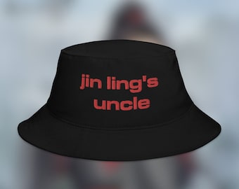 Pode incluir: Chapéu bucket preto com a inscrição "jin ling's uncle" bordada em vermelho. O chapéu tem uma aba larga e um design macio e não estruturado. O chapéu é feito de um tecido durável e é adequado para uso casual.
