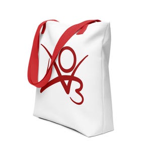 Op de afbeelding: Witte draagtas met rode handvatten en een rood grafisch ontwerp. De tas heeft een groot, gestileerd ontwerp op de voorkant. De handvatten zijn felrood en contrasteren met de witte achtergrond. Deze draagtas is geschikt voor het dragen van diverse items.
