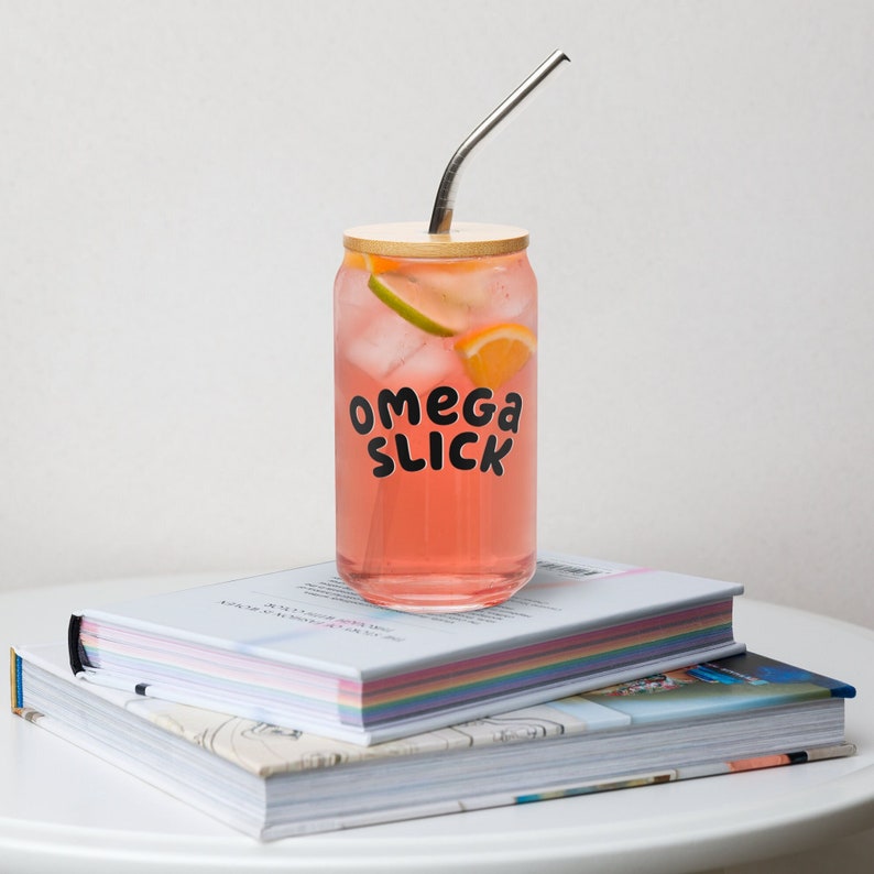 glass cup with a silver straw and wooden lid that has the words omega slick on it. perfect for omegaverse and ao3 and fanfiction fans to drink from