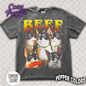 Puede incluir: Camiseta gris oscuro con un gráfico de perros de dibujos animados y la palabra "BEEF" en amarillo y naranja. Los perros son blancos y negros con collares verdes. La camiseta tiene los logotipos "Comfort Colors" y "Pepper Colors".