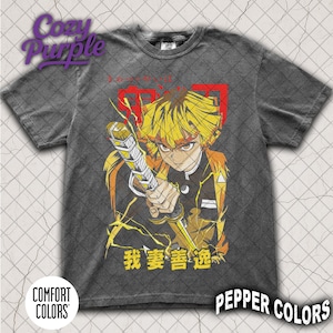 Pode incluir: Camiseta cinza escuro com uma ilustração de personagem de anime. O design apresenta uma figura de cabelo amarelo segurando uma espada, com texto japonês e detalhes em vermelho. Aparência vintage.