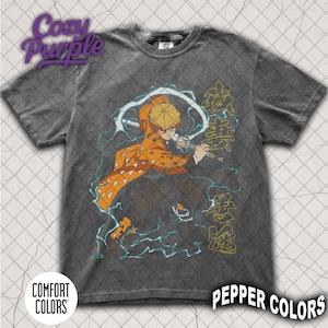 Pode incluir: T-shirt cinzenta escura com uma ilustração de personagem com detalhes em laranja e amarelo, empunhando uma espada e rodeado por raios azuis. A camisa inclui os textos "Cozy Purple", "Comfort Colors" e "Pepper Colors".