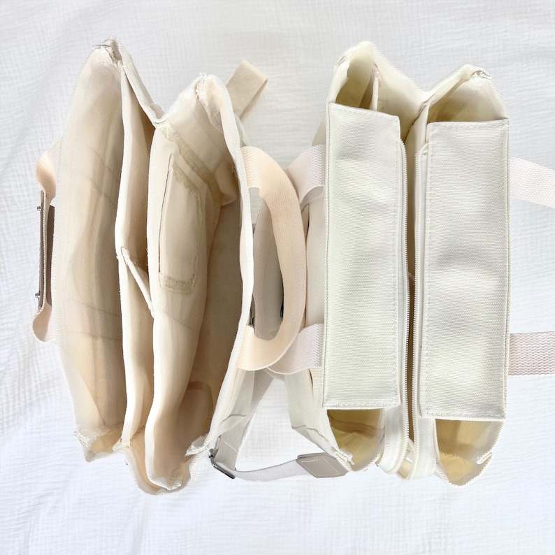 Op de afbeelding: Een cr&egrave;mekleurige, open tas met meerdere compartimenten en een vak met ritssluiting. De tas heeft beige bandjes en een neutraal kleurenpalet, wat wijst op een minimalistische esthetiek. De tas is gemaakt van een zacht, mogelijk stoffen materiaal.