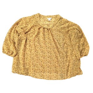 Może przedstawiać: Żółta bluzka z małym kwiatowym wzorem. Bluzka ma okrągły dekolt i rękawy do trzech czwartych. Tkanina wydaje się lekka i lekko przezroczysta.