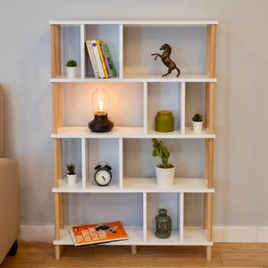 K&ouml;nnte beinhalten: Wei&szlig;es B&uuml;cherregal mit Holzbeinen und mehreren Regalbrettern. Die Regalbretter sind mit B&uuml;chern, Pflanzen, einer Lampe, einer Uhr und Dekoartikeln gef&uuml;llt.