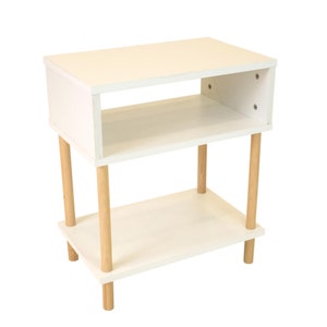 May include: White end table with two shelves and wooden legs. The table is made of wood and has a modern design.