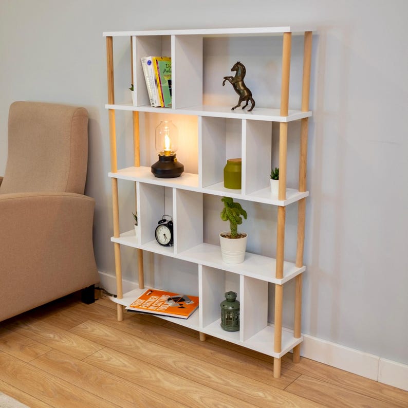 K&ouml;nnte beinhalten: Wei&szlig;es B&uuml;cherregal mit Holzakzenten und 10 Regalbrettern. Die Regalbretter sind mit B&uuml;chern, Pflanzen, einer Lampe, einer Uhr und Dekorationsartikeln gef&uuml;llt.
