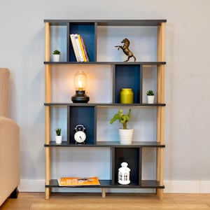 K&ouml;nnte beinhalten: Ein Holzregal mit dunkelgrauer Oberfl&auml;che und hellen Holzakzenten. Die Regalb&ouml;den sind in F&auml;cher unterteilt und zeigen verschiedene Dekorationsartikel, darunter eine Lampe, eine Uhr, eine Pferdefigur und Topfpflanzen.