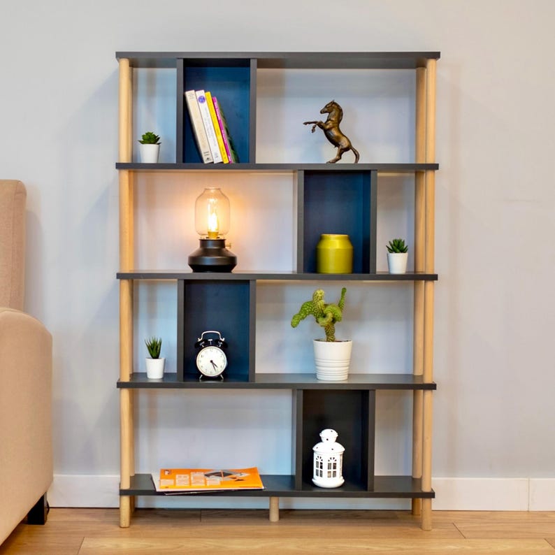 K&ouml;nnte beinhalten: Ein Holzregal mit dunkelgrauer Oberfl&auml;che und hellen Holzakzenten. Die Regalb&ouml;den sind in F&auml;cher unterteilt und zeigen verschiedene Dekorationsartikel, darunter eine Lampe, eine Uhr, eine Pferdefigur und Topfpflanzen.