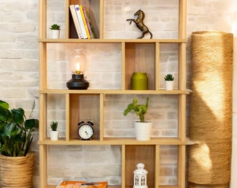 Peut inclure: Une étagère en bois avec plusieurs compartiments, présentant une variété d'objets décoratifs, notamment des livres, des plantes, une lampe, une horloge et une lanterne. L'étagère est en bois clair et a une finition naturelle.