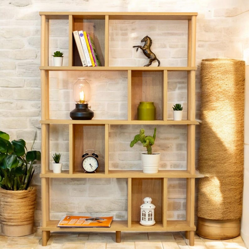K&ouml;nnte beinhalten: Ein Holzregal mit mehreren F&auml;chern, das mit verschiedenen Dekorationsartikeln ausgestattet ist, darunter B&uuml;cher, Pflanzen, eine Lampe, eine Uhr und eine Laterne. Das Regal ist aus hellem Holz gefertigt und hat eine nat&uuml;rliche Oberfl&auml;che.