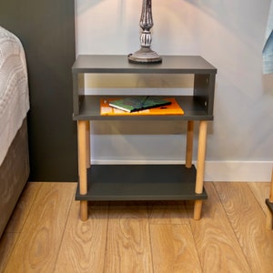 May include: A dark gray nightstand with two shelves and wooden legs. A book is on the top shelf.