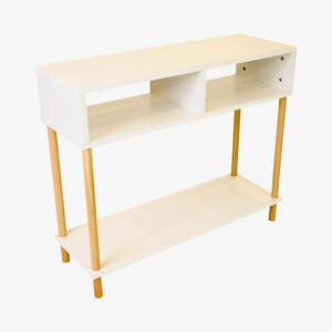 May include: White console table with two shelves and four wooden legs. The table has a modern design and is perfect for a living room or entryway.