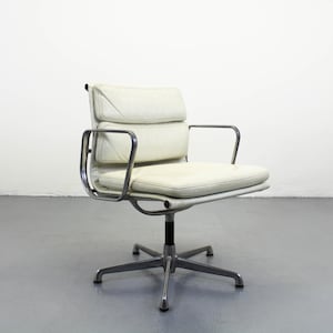 May include: Cream-colored office chair with a low back and armrests. The chair has a padded seat and backrest, and a chrome-colored frame and base. The chair is designed for comfort and style.