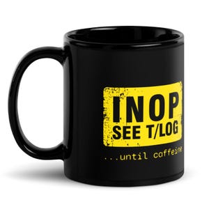 以下が含まれることがあります： 「INOP SEE T/LOG ...until caffeine」と書いてある黄色い正方形のグラフィックが描かれた黒いセラミック製のコーヒーカップです。