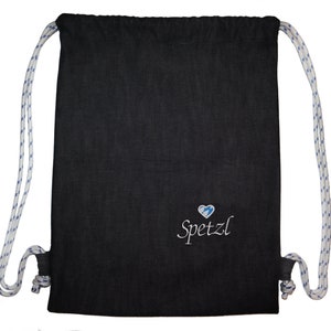 以下が含まれることがあります： 白と青の紐が付いた黒い巾着袋。袋には青い稲妻が入った白い刺繍のハートと、その下に「Spetzl」という文字が刺繍されている。