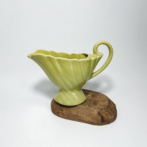 Puede incluir: Una salsera de cerámica verde con un diseño acanalado y un asa. La salsera está sobre una base de madera.