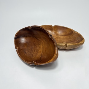 Pode incluir: Duas tigelas de madeira, uma com uma forma redonda e lisa e a outra com uma forma mais oval. Ambas as tigelas são feitas de madeira marrom escura e têm um aspecto natural e rústico.