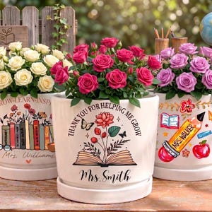 May include: Three white ceramic flower pots filled with roses in shades of white, pink, and purple. Each pot is decorated with a teacher-themed design and the names "Mrs. Williams", "Mrs. Smith", and "Mrs. Walker".
