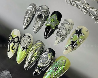 Op de afbeelding: Een set van tien groene en zilveren nagelontwerpen met sterren, swirls en strikken. De ontwerpen zijn op een zilveren achtergrond.