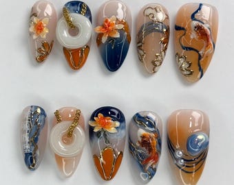 May include: Set of ten false nails with a variety of designs featuring koi fish, flowers, and jade pendants. The nails are painted in shades of blue, orange, and white.