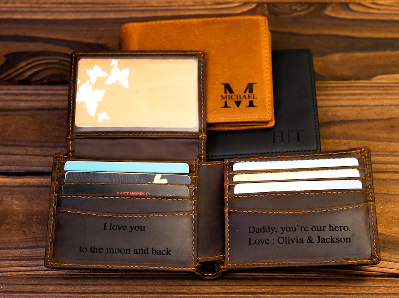 Puede incluir: Una cartera de cuero marr&oacute;n con m&uacute;ltiples ranuras para tarjetas y un mensaje personalizado. La cartera tiene una solapa con un dise&ntilde;o de mariposa y un bolsillo separado para efectivo. El mensaje en la cartera dice "Te amo hasta la luna y de regreso" en un lado y "Pap&aacute;, eres nuestro h&eacute;roe. Amor: Olivia & Jackson" en el otro.
