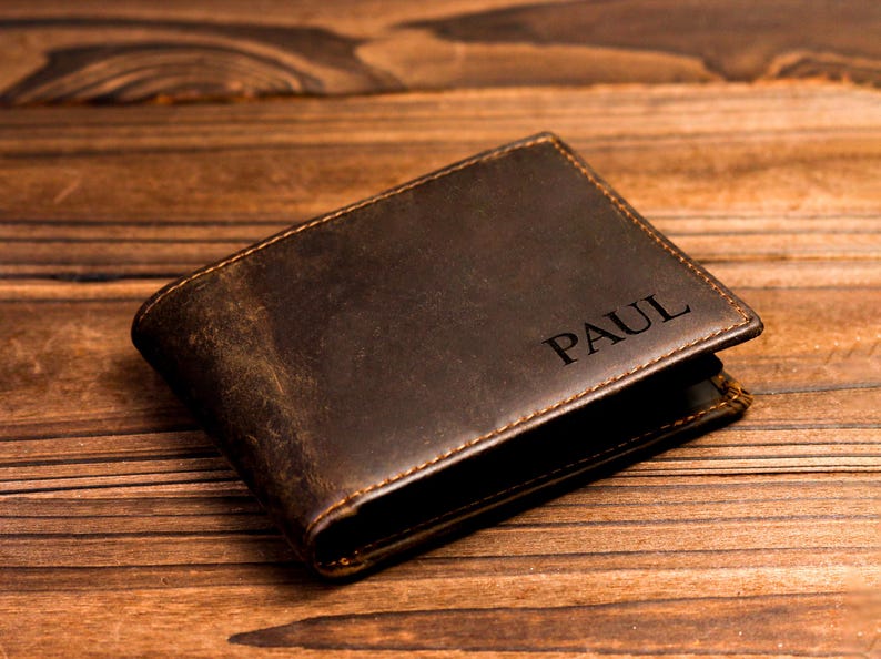 Puede incluir: Una cartera de cuero marr&oacute;n con el nombre "PAUL" grabado en la parte delantera.