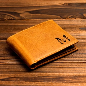 Puede incluir: Una cartera de cuero marr&oacute;n con el nombre "MICHAEL" y la inicial "M" grabada en la parte delantera.