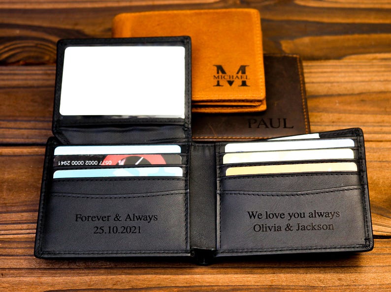 Puede incluir: Dos carteras de cuero negro con ranuras para tarjetas y grabados personalizados. Una cartera dice "Forever & Always 25.10.2021" y la otra dice "We love you always Olivia & Jackson".