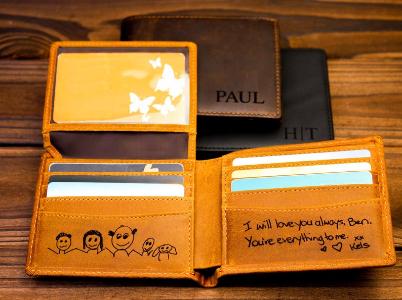 Puede incluir: Una cartera de cuero marr&oacute;n con una inscripci&oacute;n personalizada y un dibujo de una familia. La cartera tiene m&uacute;ltiples ranuras para tarjetas y un portafolios. La inscripci&oacute;n dice "I will love you always, Ben. You're everything to me. xx Kels."