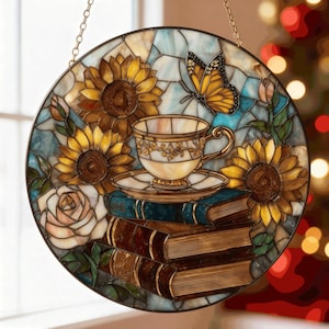 May include: Round stained glass panel featuring a teacup and saucer atop a stack of books, surrounded by sunflowers, a butterfly, and a rose. The panel has a gold chain for hanging and is set against a light blue and white background.