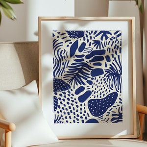 May include: A framed art print featuring a cream-colored background with a repeating pattern of navy blue organic shapes. The shapes include dots, lines, and leaf-like forms. The artwork is displayed in a light wood frame.