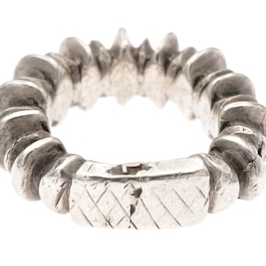 Può includere: Un anello d'argento con un design testurizzato e rigato. L'anello è composto da una serie di piccoli pezzi sovrapposti che creano un motivo unico e intricato.
