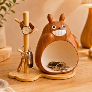 May include: A wooden desk organizer featuring a tree-shaped stand with a watch and keychains, alongside a smooth, brown, rounded creature-shaped storage bowl with a white interior containing a set of keys, all set on a connected wooden base.