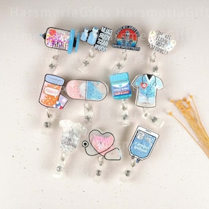 May include: Assortment of colorful, glittery, and themed badge reels.  The reels feature various designs including a syringe, a pill bottle, a stethoscope, a heart, and a hospital bag.  The text on the reels includes "Calm Your Sass Down", "It's Fine I'm Fine Everything is Fine", "Helping Healing", "I Heart My Mamas", and "Baby Bad?"