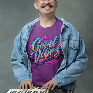 May include: A person wearing a purple t-shirt with the text "Good Vibes" in colorful lettering, a blue denim jacket, and colorful patterned pants, playing a black keyboard.